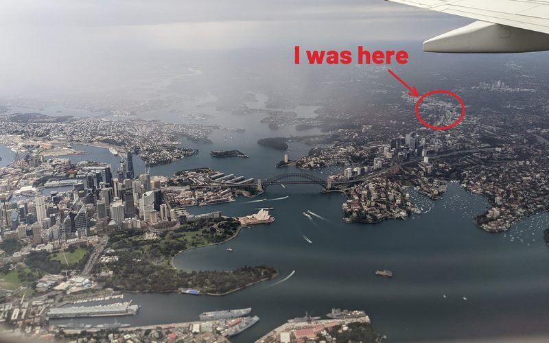 Sydney from a plane window, the Harbour Bridge below, with St Leonards circled in red and the words I was here